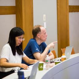 Jim Fill and Henning Sulzbach talking, while Emma Yu Jin and Sam Simon work on their laptops.